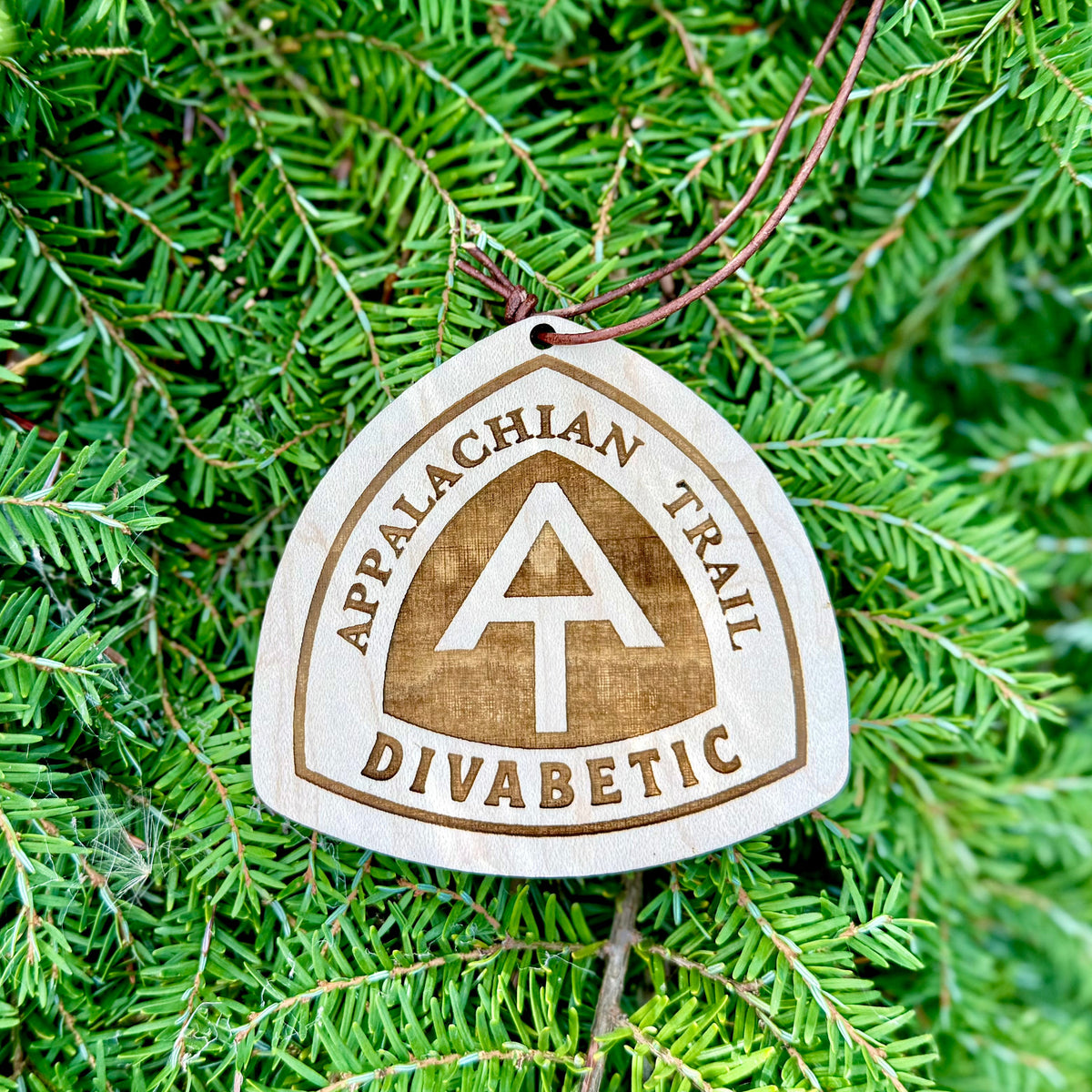 Close-up of an engraved Appalachian Trail wooden hangtag against dense evergreen foliage