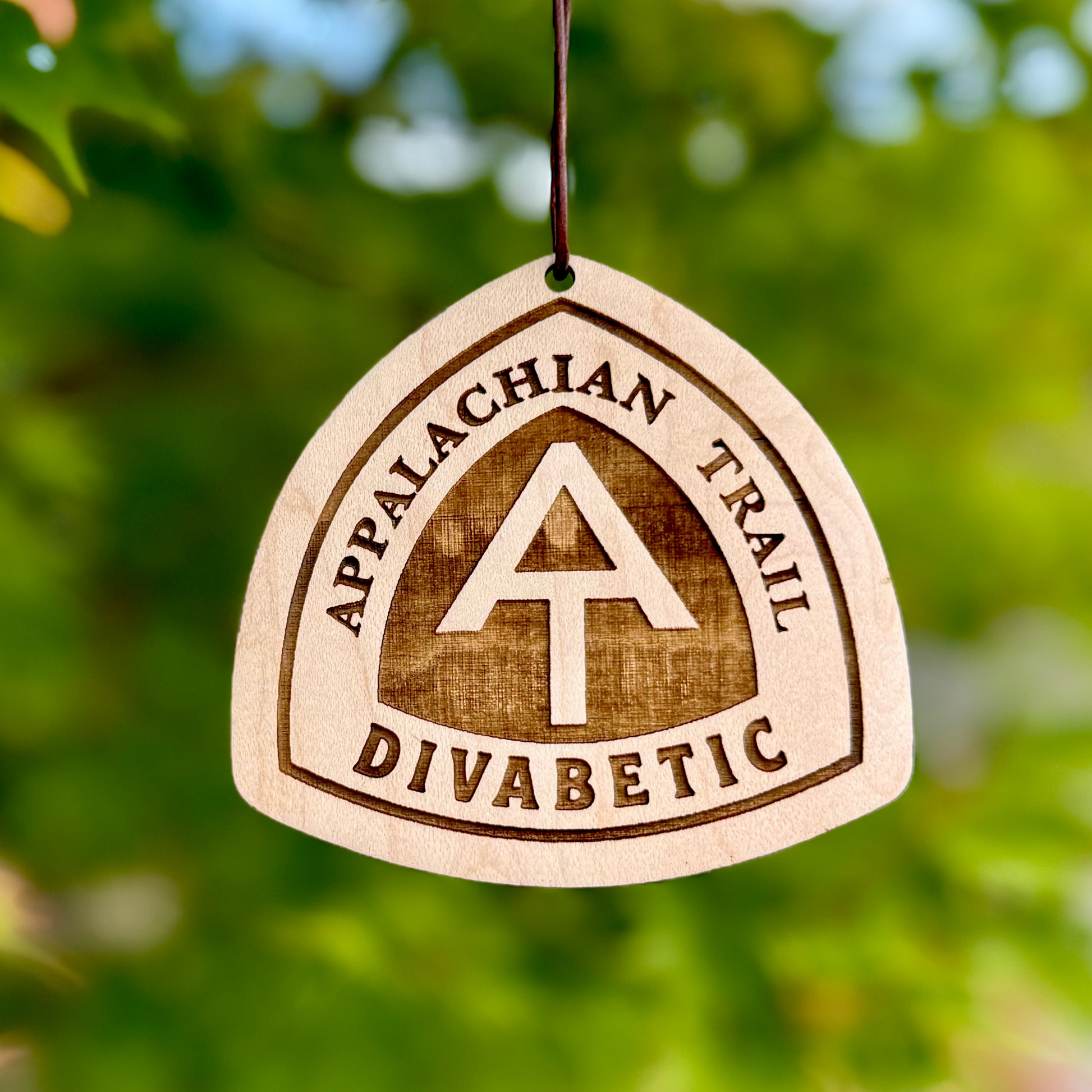 Close-up of an engraved Appalachian Trail wooden tag hanging among green leave