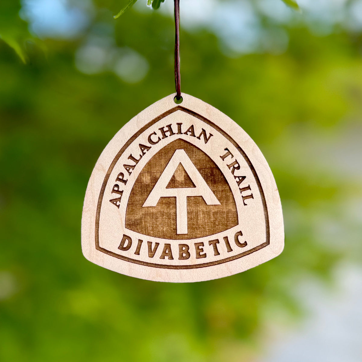 Engraved Appalachian Trail hangtag photographed against a soft green outdoor background