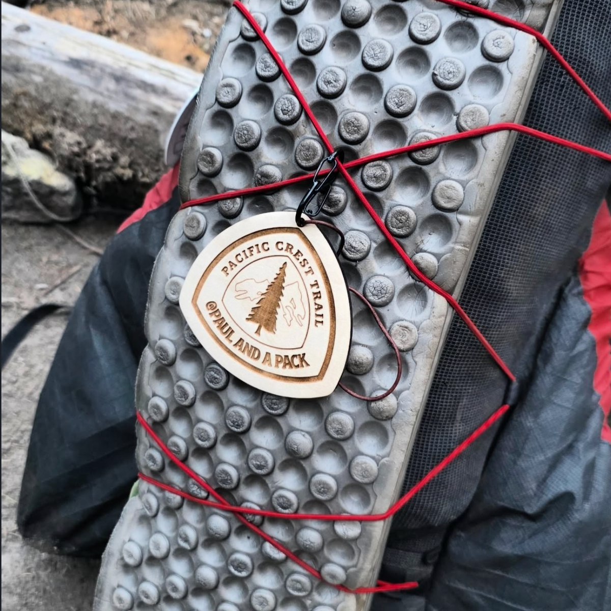 Lightweight wooden trail name tag clipped to a backpack for hiking
