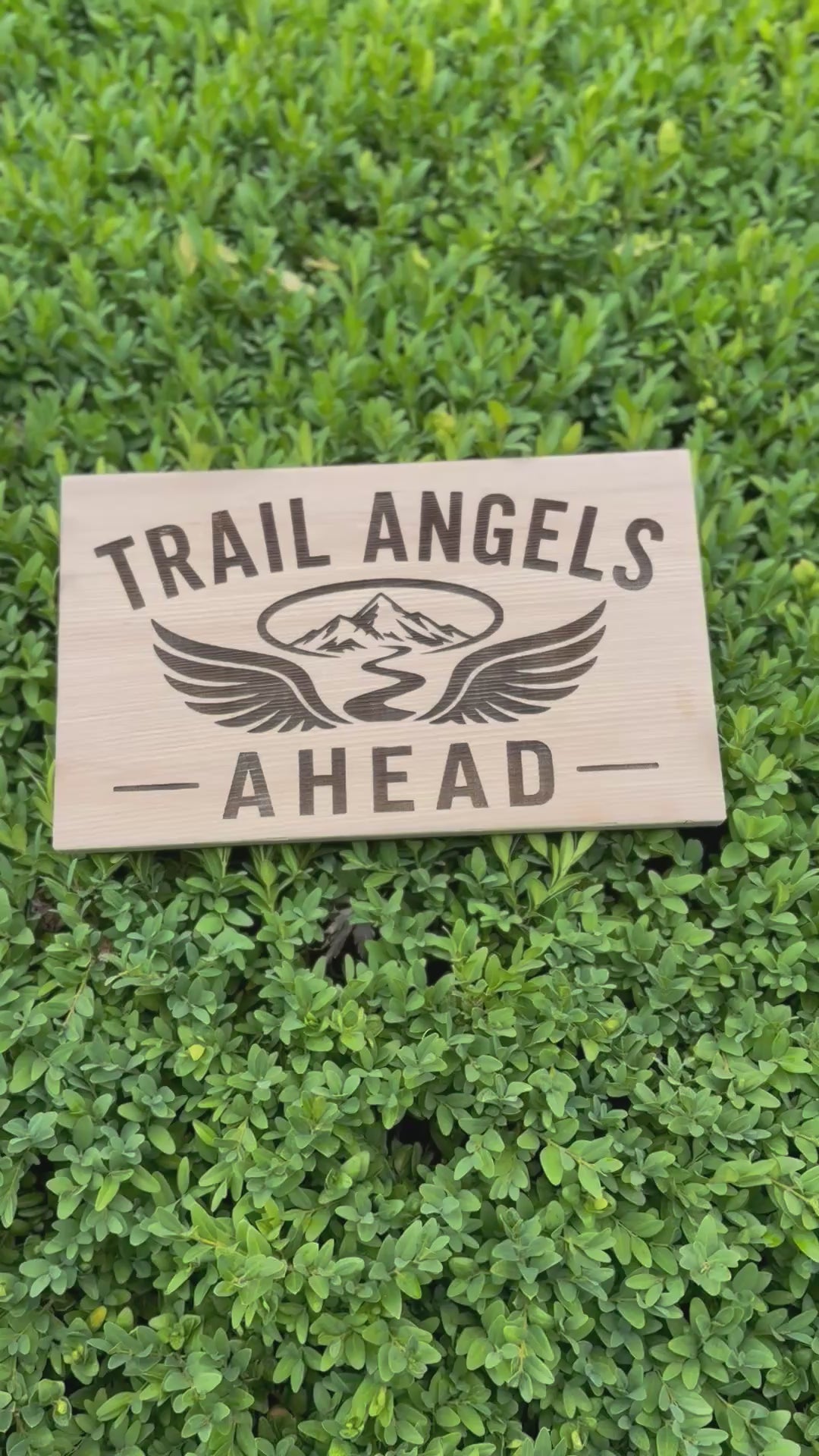 Trail Angels Ahead wood sign on a forest tree with hikers enjoying breakfast and trail magic in the background