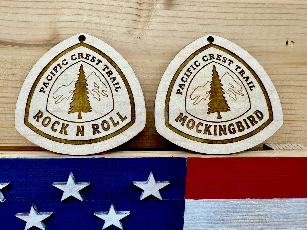 Two engraved wooden hiking tags displayed together above a decorative background