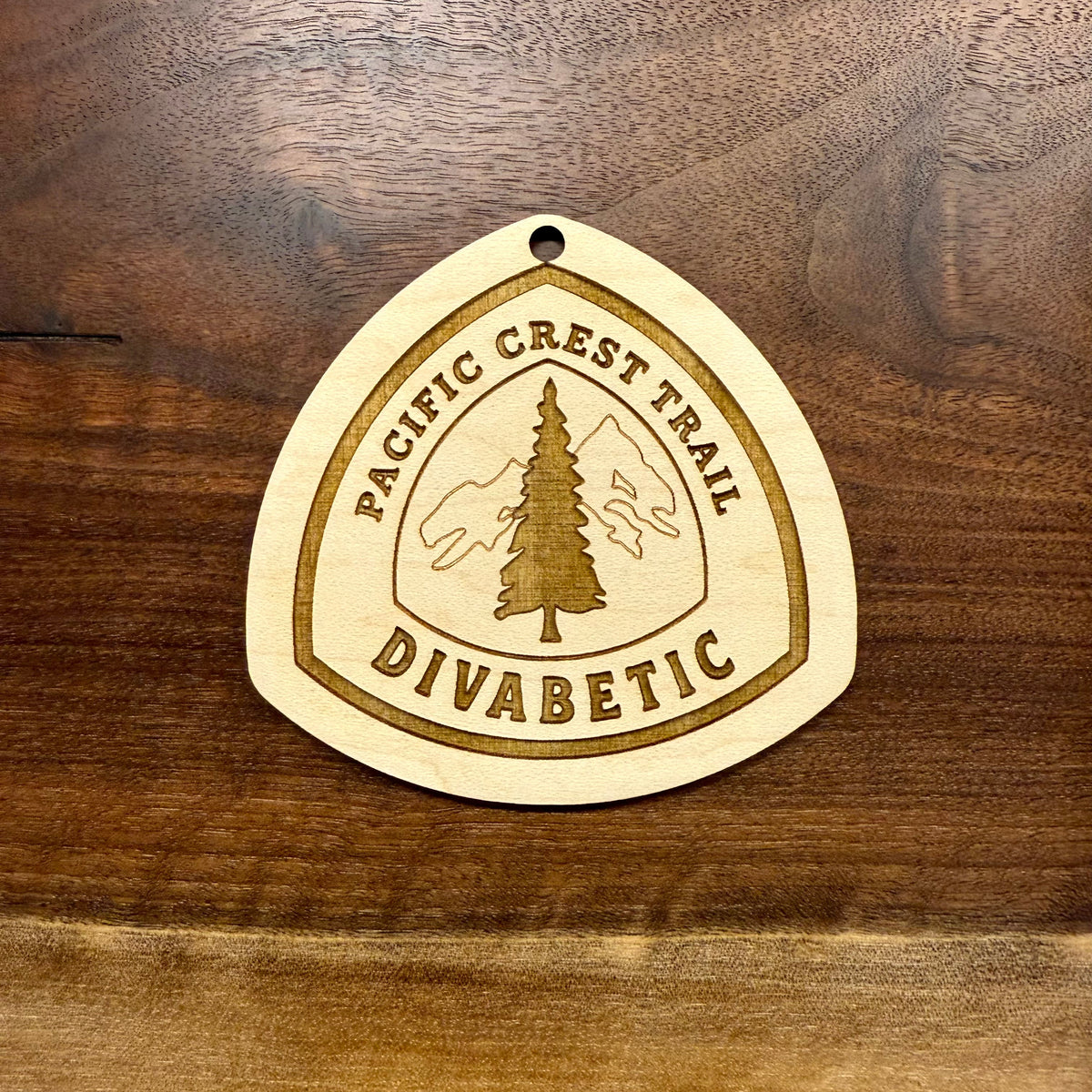 Close-up of the engraved design and natural wood grain on a hiking tag
