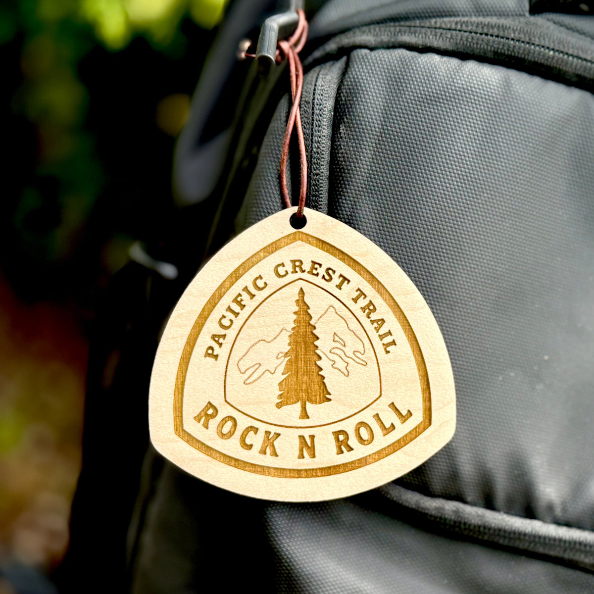 Wooden trail name tag hanging from the strap of a hiking backpack